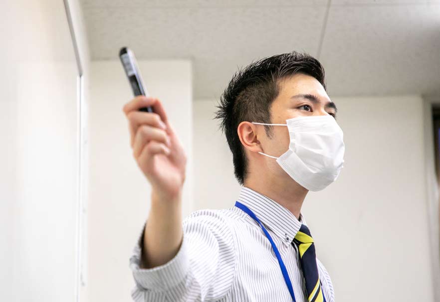 ホワイトボードを指しながら生徒に問いかける講師